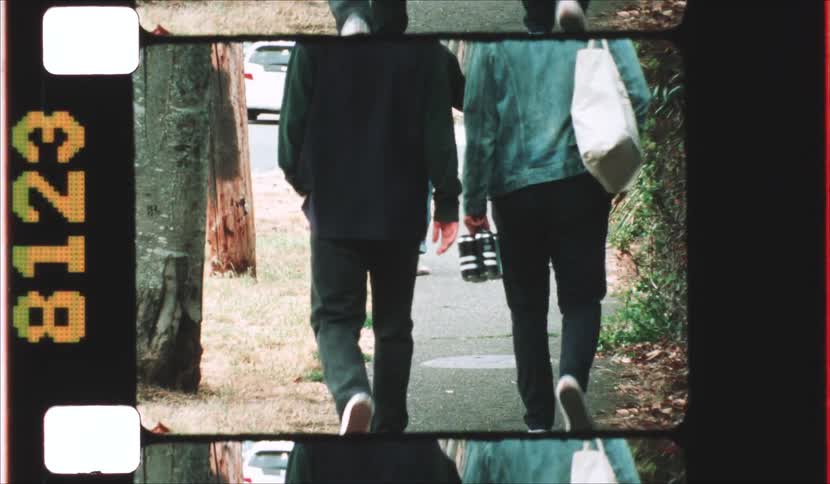 A view from behind shows a group of friends walking down a paved sidewalk lined with trees and greenery presented within a vintage film strip frame with visible grain and sprocket holes