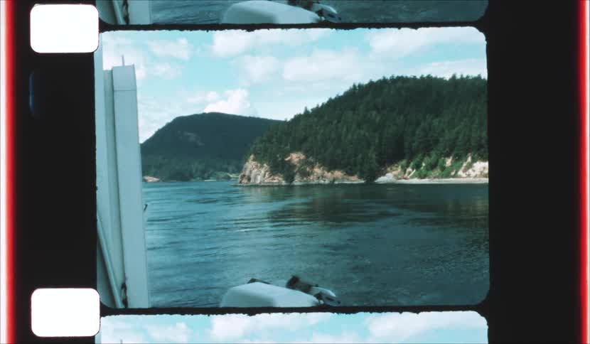 A view from a boat shows calm water and forested hills along a rocky coastline framed within a vintage film strip