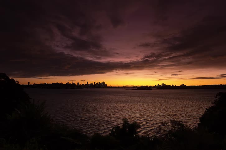 A time lapse of the sydney skyline and harbor bridge during sunset as the sky turns from orange to dark purple