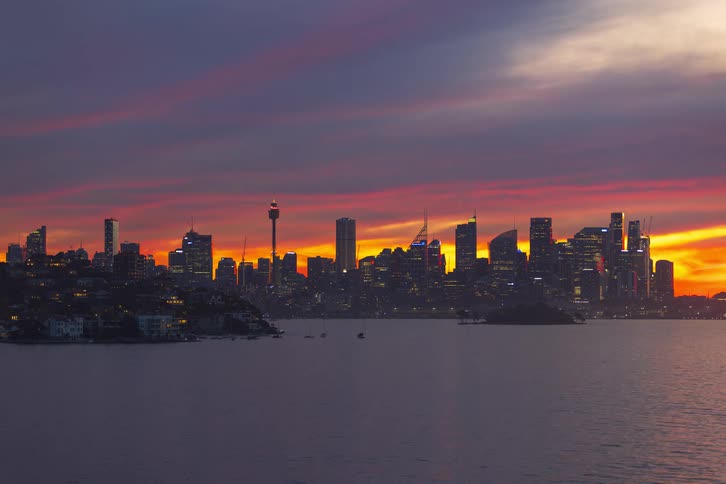 Metropolitan buildings and skyscrapers on the sydney australia skyline on the coast as boats sail on the water and city lights glow as darkness falls