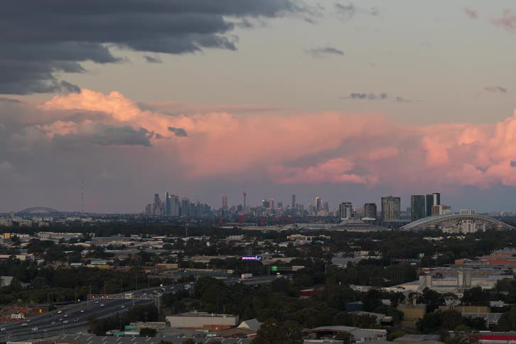 A wide shot time lapse of the sydney skyline transitioning from a cloudy afternoon to night with highway traffic in the foreground