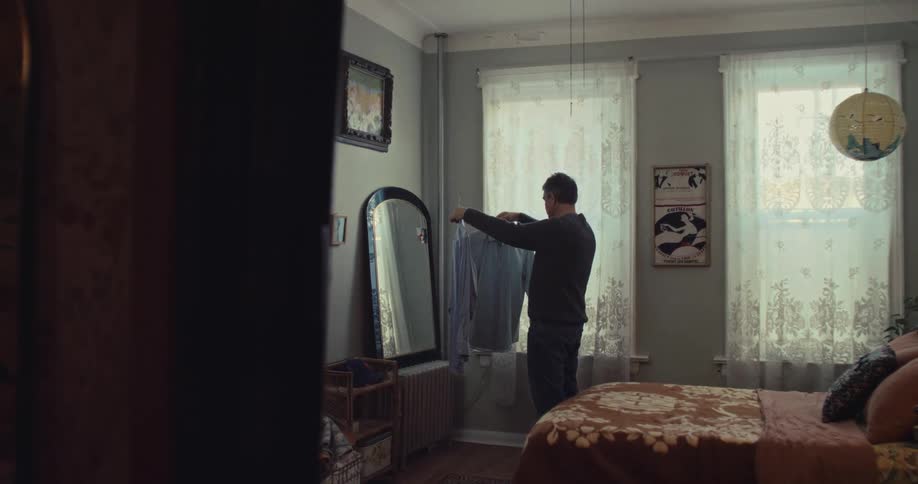 A man holding and choosing between two shirts while standing in front of a mirror in a bedroom