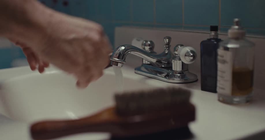 A person reaches for a bathroom faucet and turns the handle to start the water they briefly rinse their hands under the stream before turning the water off