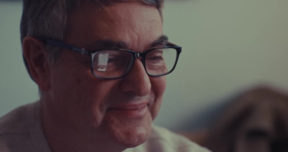 Man wearing glasses smiles while looking at phone screen reflected in lenses