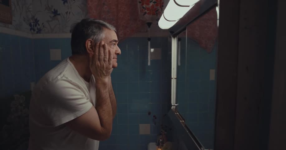 A man smiles as he rinses his face in front of a bathroom mirror