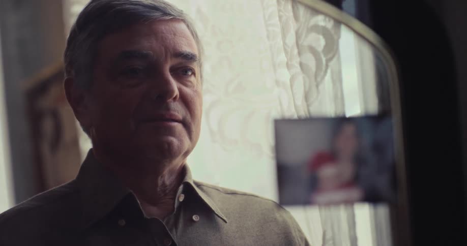 Man buttons shirt while looking at his reflection in mirror with photograph attached to the edge
