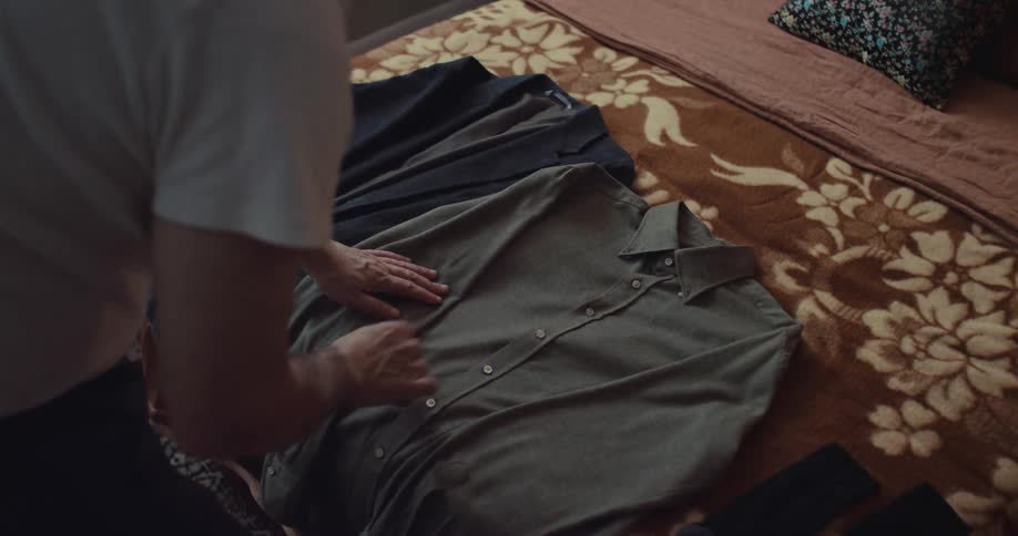 Man lays out a shirt and jacket on his bed