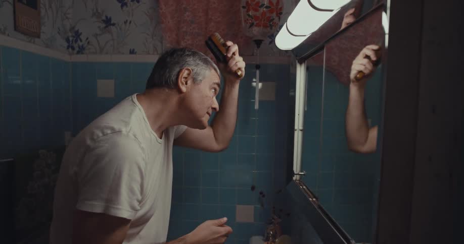 A middle aged man brushing his hair while looking into a vanity mirror in a bathroom