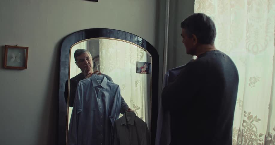 A man choosing a casual outfit while standing in front of a mirror in a bedroom