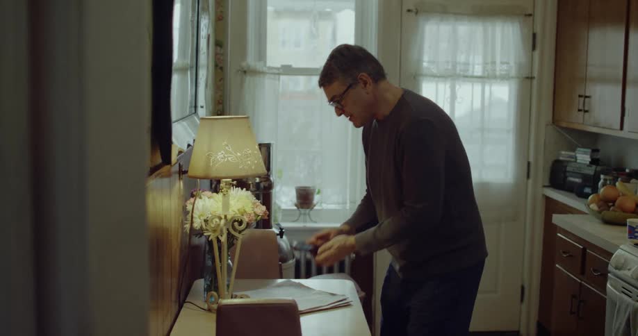 A man in his kitchen turns to look at his phone and acts relieved