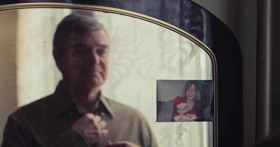 Man buttons shirt in front of mirror with photograph attached on the side