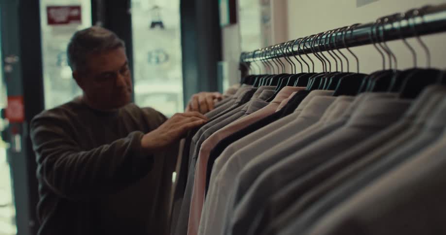 A man browsing through a rack of button down shirts in a clothing store