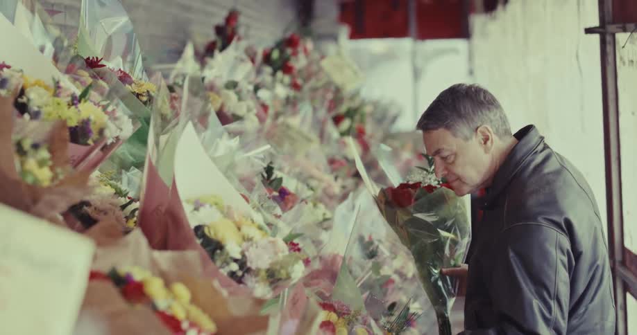 A man choosing a bouquet while rows of wrapped flowers are displayed in a flower shop