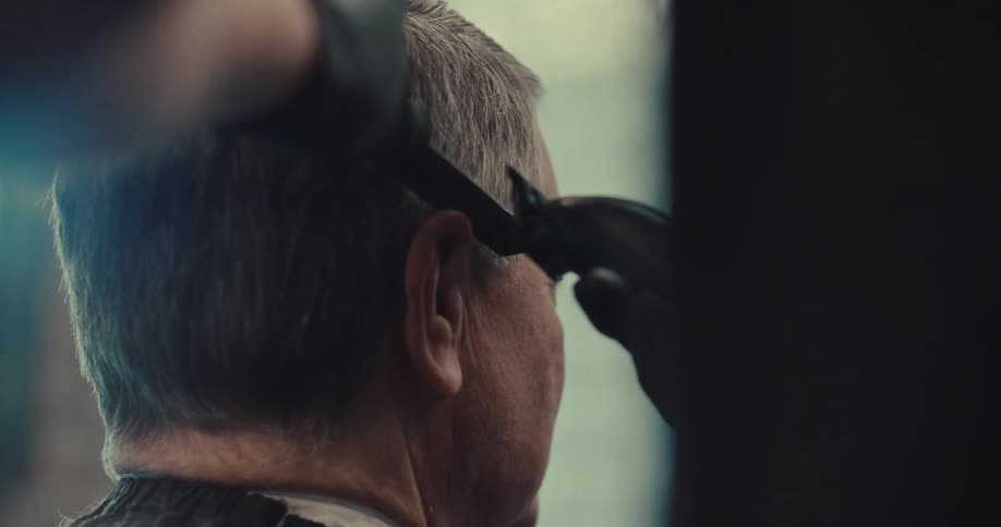 Barber uses electric clipper to trim hair of man seated in chair
