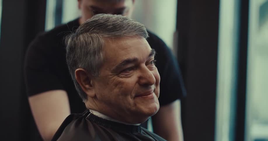 Man smiles as he sits in the barbershop getting his hair cut