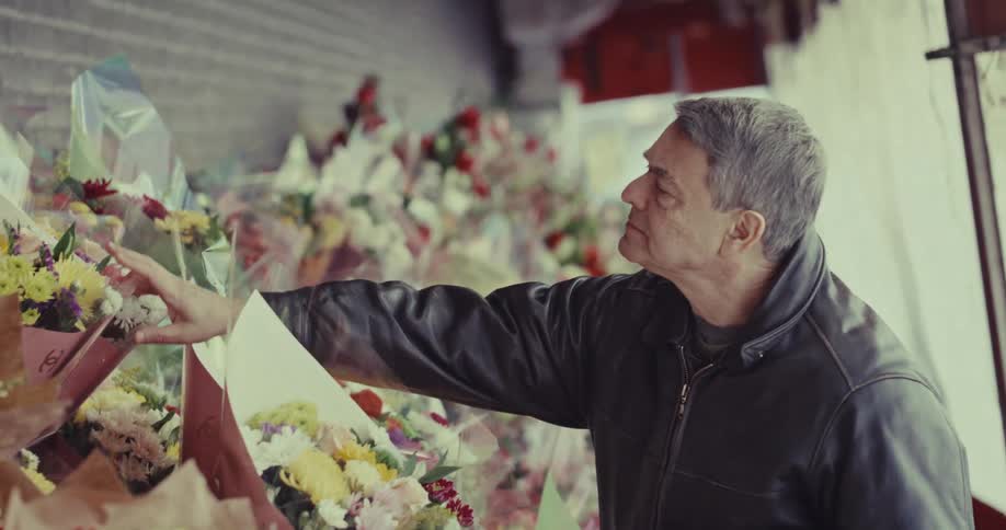 A middleaged man in a black leather jacket thoughtfully examines a vibrant display of flower bouquets at an outdoor market he gently reaches out to touch the colorful petals while deciding which arrangement to select