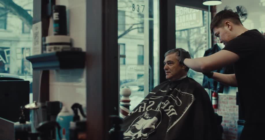 Barber uses electric clipper to trim hair of client seated in chair inside barbershop