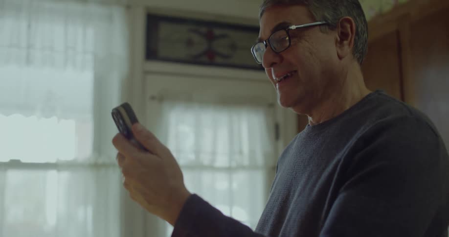 Man wearing glasses holds phone while looking at the screen indoors