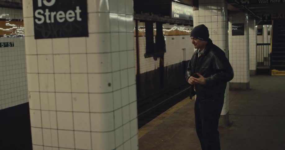 Man looks at phone while waiting on platform at 15 street subway station