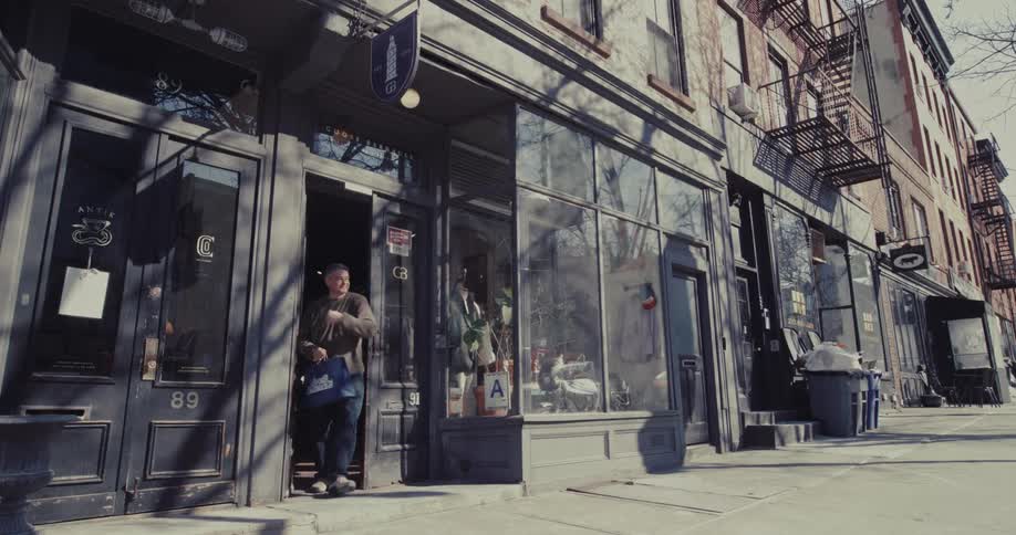A man exits a boutique clothing store carrying a shopping bag onto a sunny metropolitan sidewalk