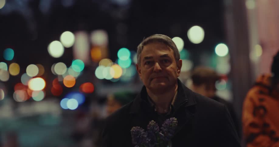 Man standing on a downtown street holding a bouquet of flowers and people and traffic move around him