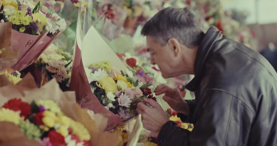 Man stands at a floral display with bouquets of flowers as he smells and touches them
