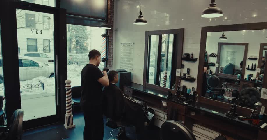 A barber cuts a mans hair with clippers inside a barbershop