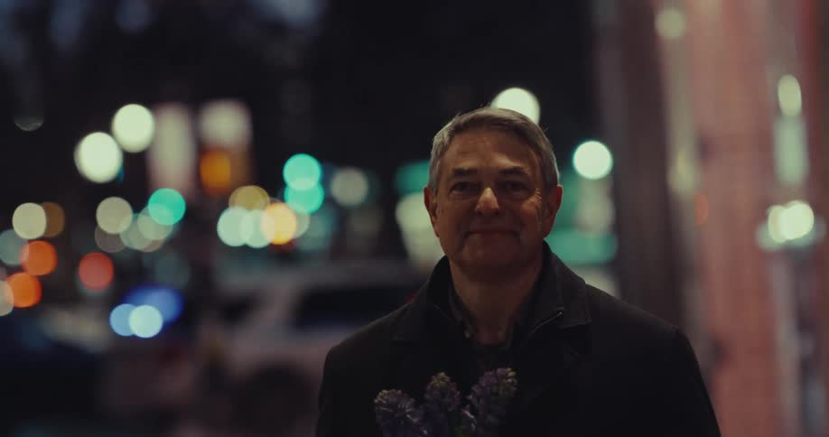 The man is holding flowers in the city at night