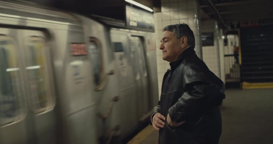 A man waiting while standing on a metropolitan subway platform as a train pulls into the station