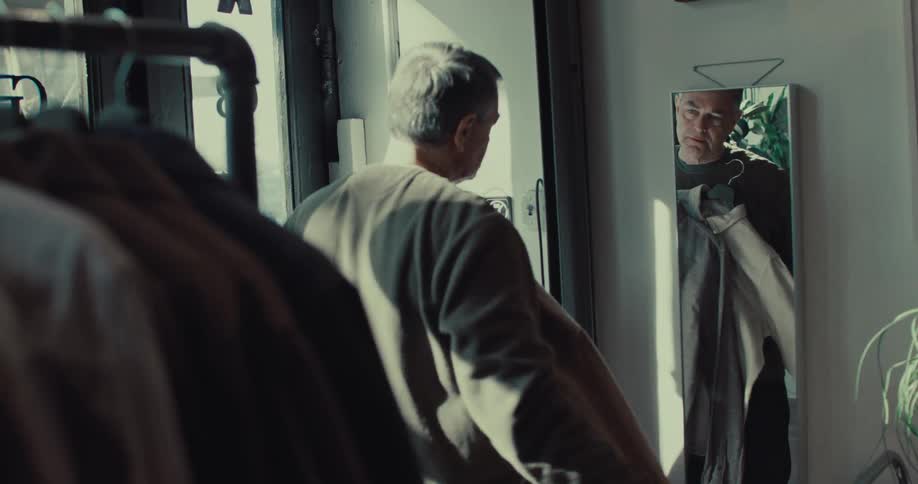 Man holds shirt in front of mirror while looking at himself inside shop