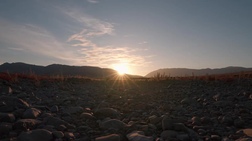 A landscape view of the sun rising over distant mountains with a rocky foreground