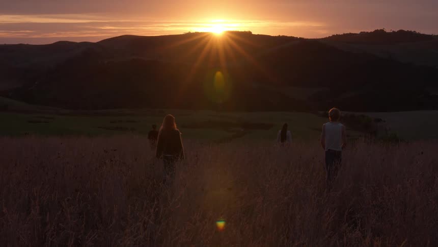 Four people walking across a grassland looking at the setting sun over the mountains