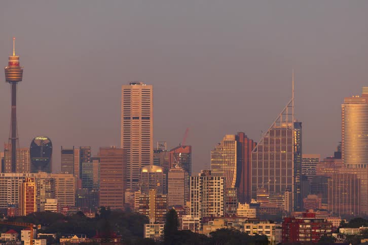 Rising sun illuminates urban skyline with skyscrapers under clear sky