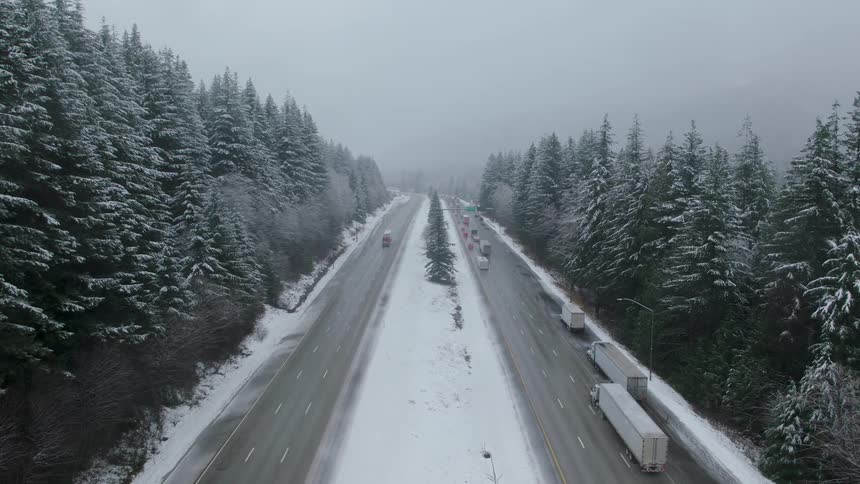 Semi trucks chain up on the side of a mountain highway as heavy traffic starts to back up heading up the pass