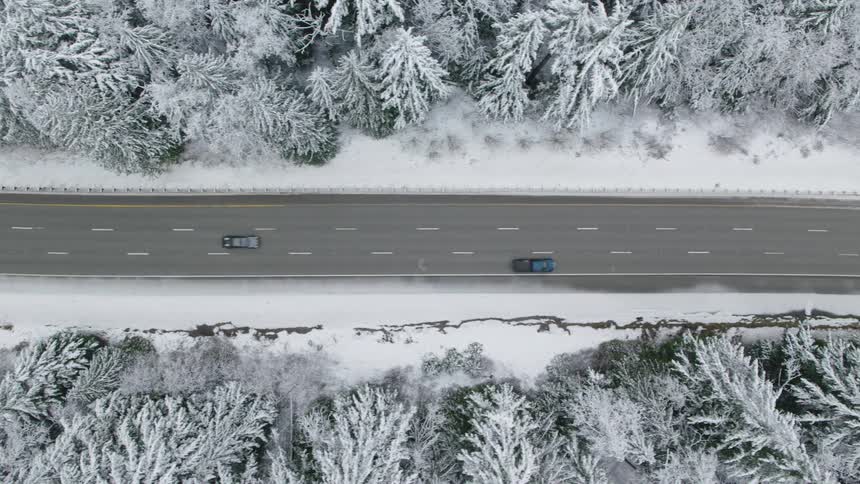 Traverse above vehicles driving on a three lane highway through a snow covered forest