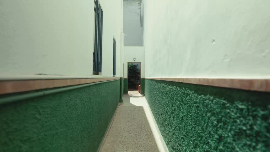 Narrow corridor between white and green walls leading to an open door lit in the background
