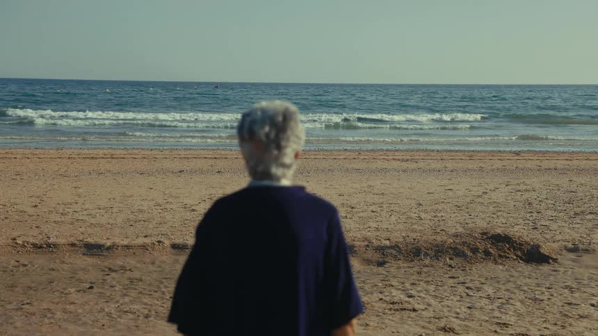 Elderly woman sitting on the beach watching waves roll into shore