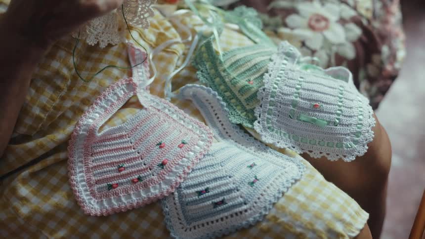 Two delicate handmade bibs resting on a persons lap they feature intricate crochet work with pastelcolored stripesone in light pink and the other in mint greenand are adorned with tiny embroidered floral details