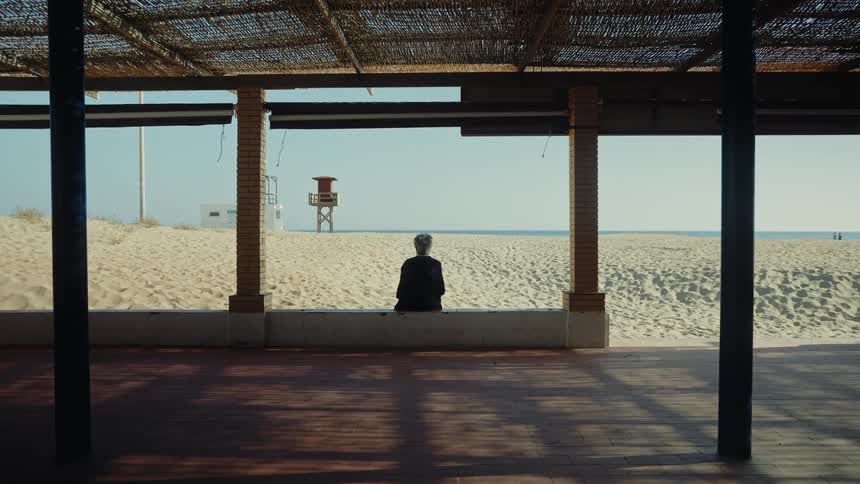 Woman sits in front of a pavilion at the beach