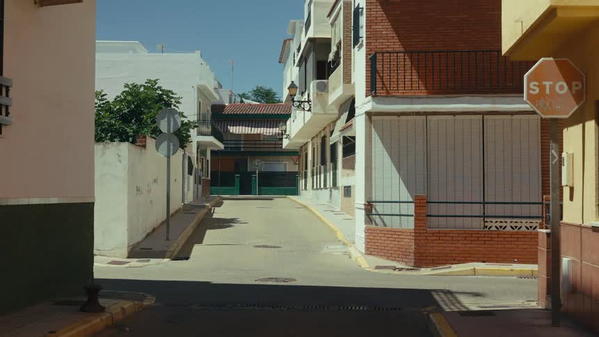 A narrow residential street features multi story houses and a white car driving in the distance