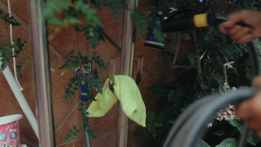 Hand holding a coiled hose on a metal holder among plants and flowers
