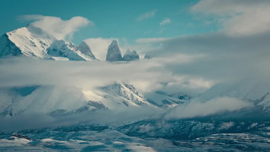 Snowcovered mountains partially surrounded by clouds under a blue sky