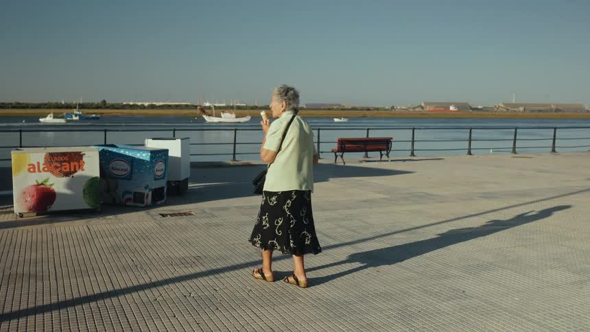 Elderly woman eating an ice cream cone as she walks on the boardwalk along coast