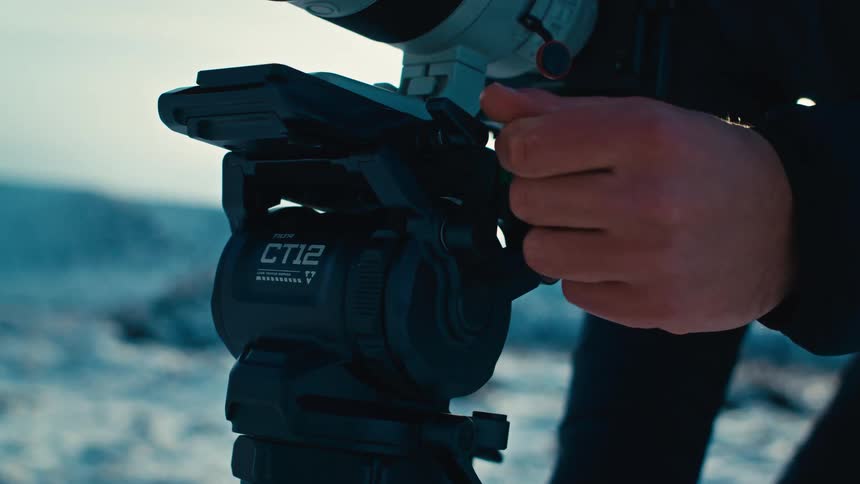Hand adjusting a camera tripod head in an outdoor setting