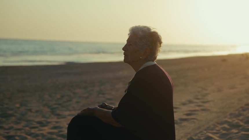 Elderly woman sitting on the beach watching waves roll into shore