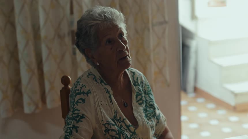 The elderly woman is listening intently and occasionally responding while engaged in a conversation with someone off camera