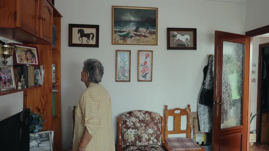 Elderly woman walking in a room with framed pictures on the wall