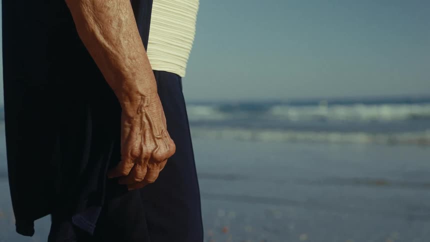 A closeup of an elderly persons weathered hand bathed in sunlight on a beach