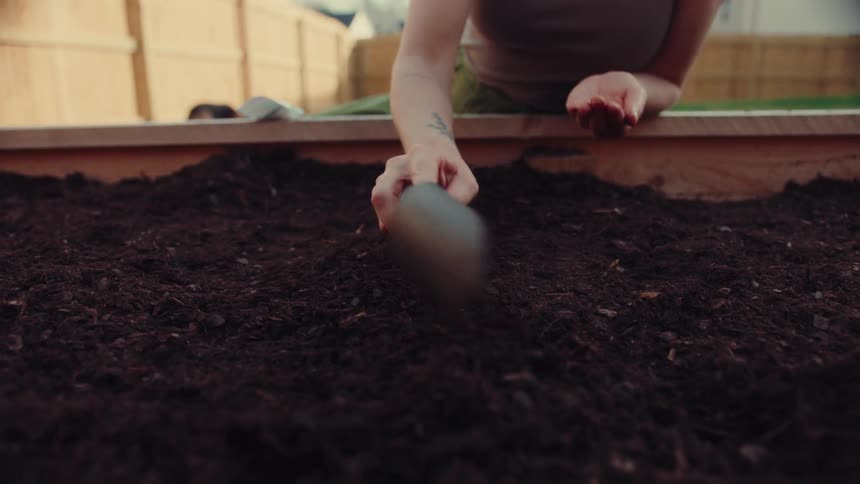 Person using a garden trowel to spread soil in a raised garden bed