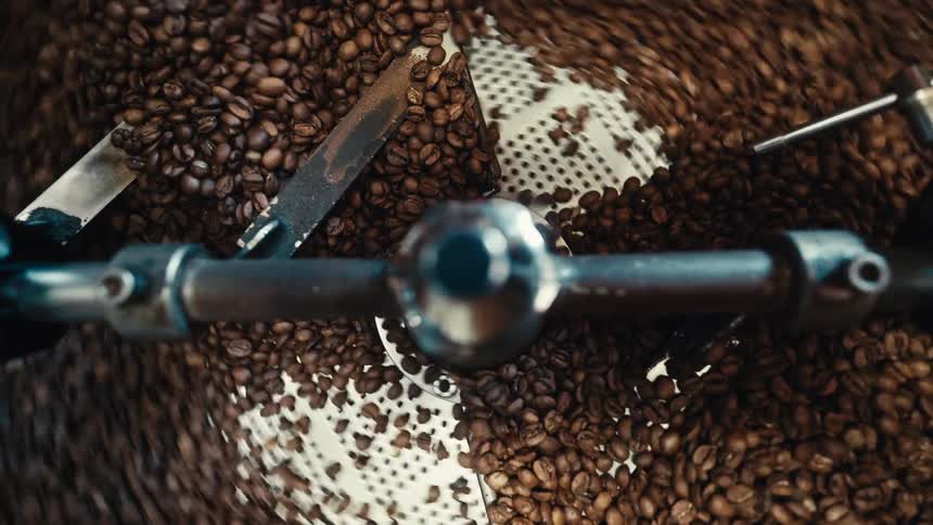 A coffee grinder grinding a series of coffee beans as the gears spin causing the beans to move around inside the machine